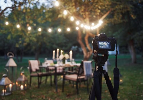 Professional equipment. Camera on the tripod stand in the field in front of prepared table at evening time.